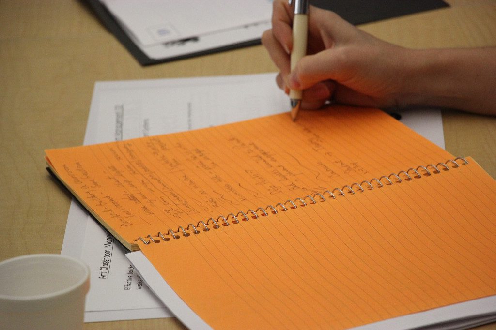 A person writing in an orange notebook.