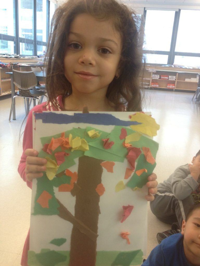 A little girl holding up a paper tree.