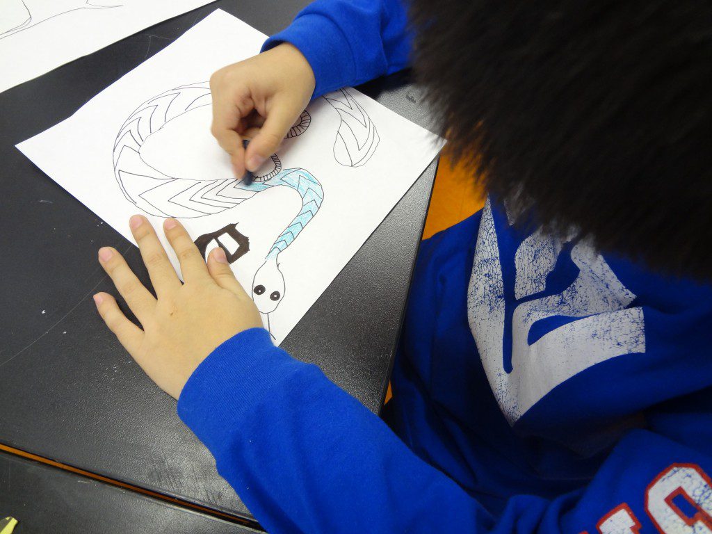 A boy drawing a snake on a piece of paper.