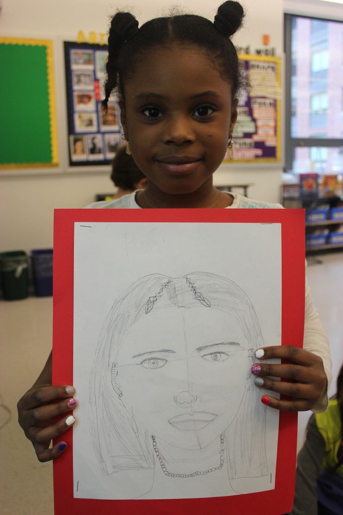 A young girl holding up a drawing of a woman.