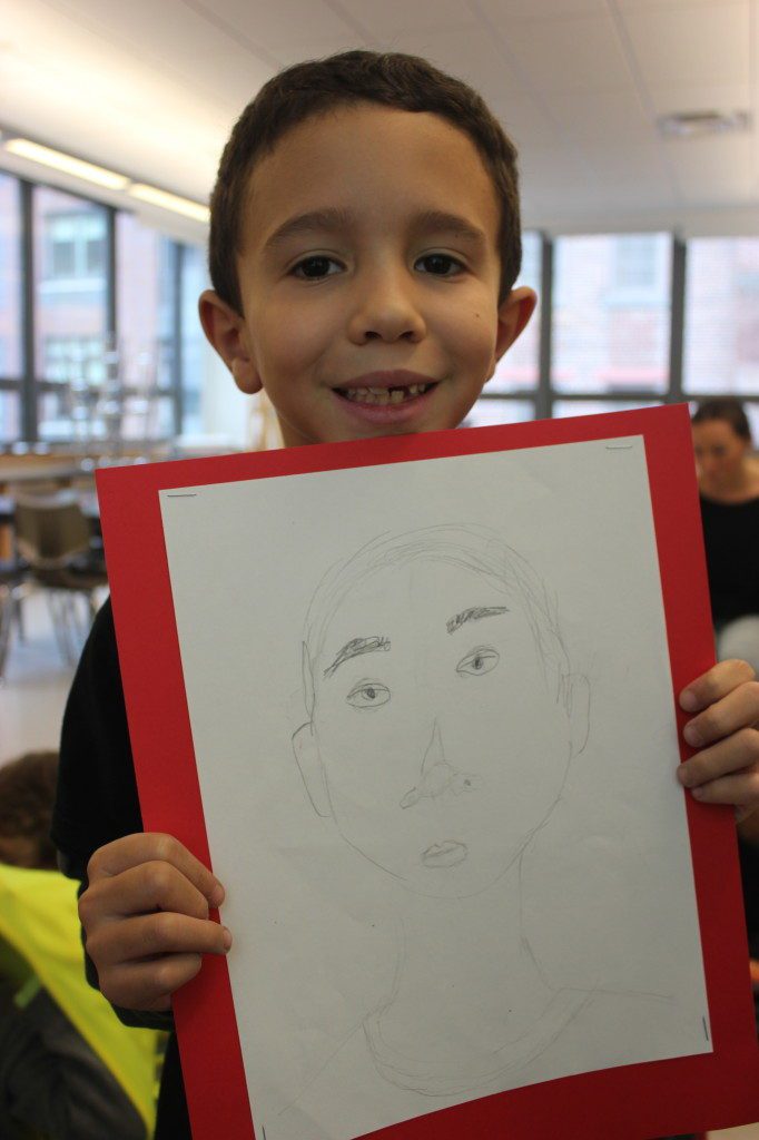 A young boy holding up a drawing of his face.