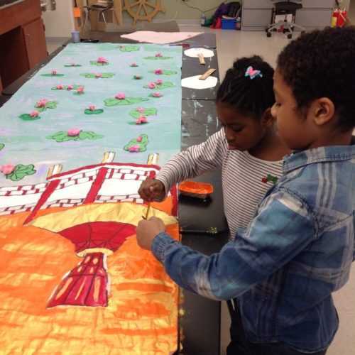 Two toddlers painting an art with orange color