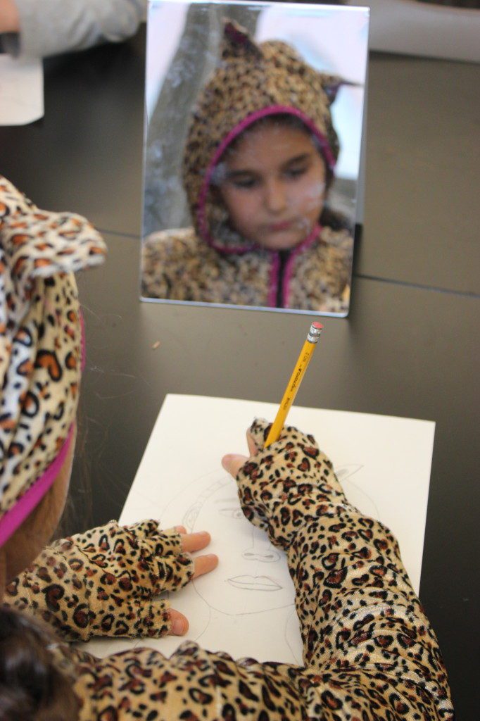 A girl in a leopard costume drawing in front of a mirror.