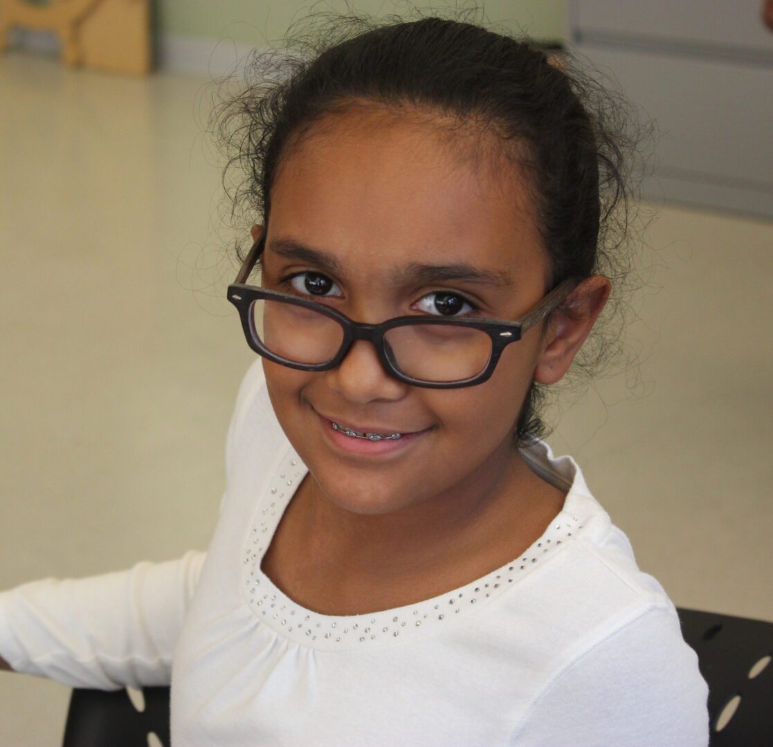 A young girl wearing glasses is sitting in a chair.