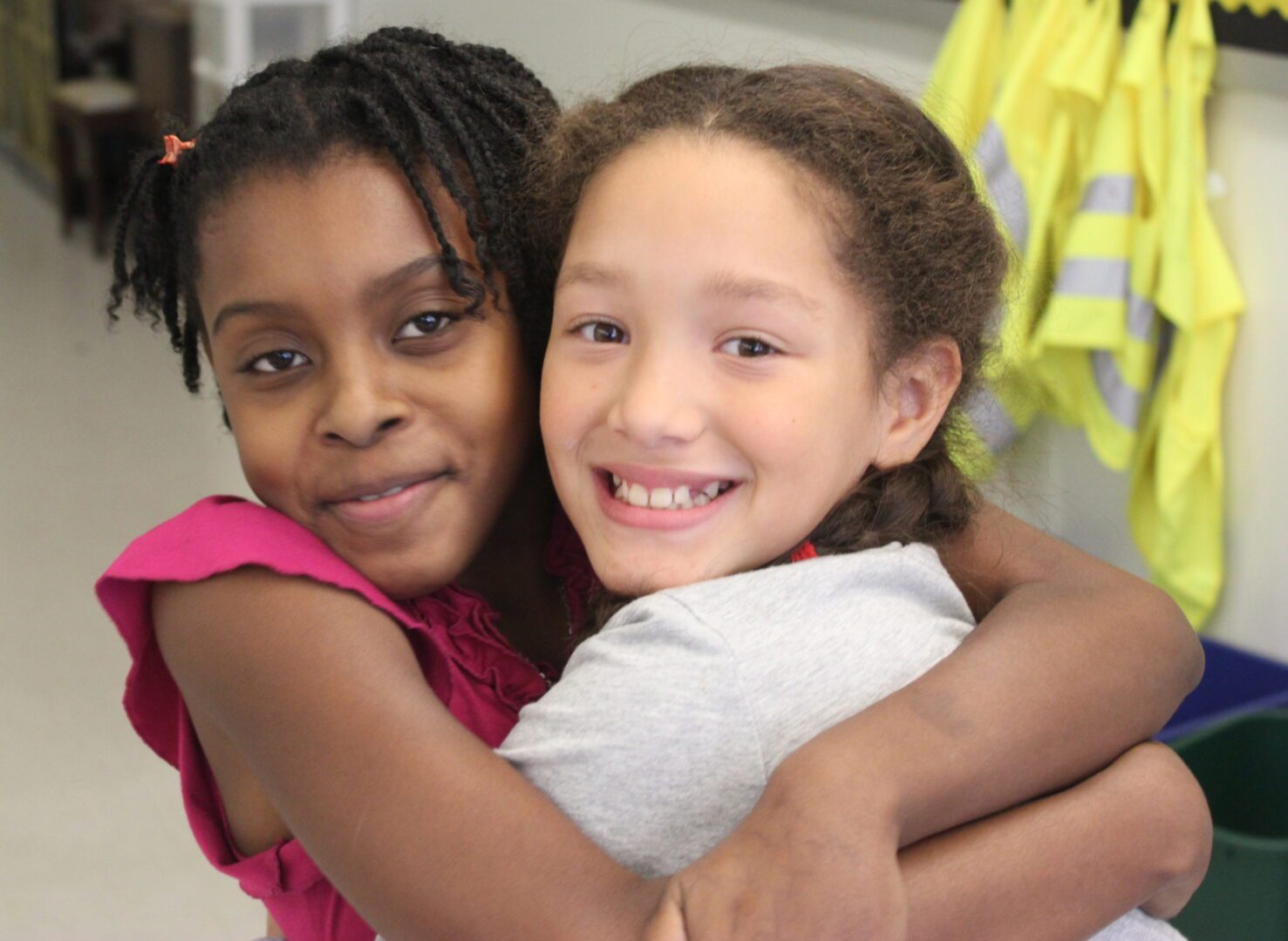 Two young girls hugging each other in a classroom.