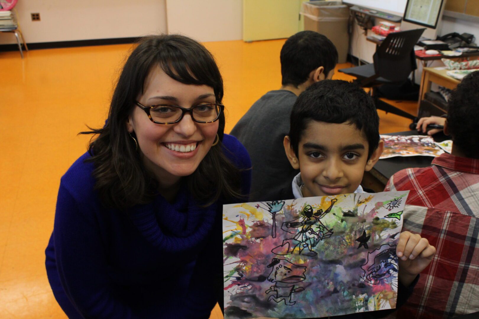 A woman holding a child's painting in a classroom.