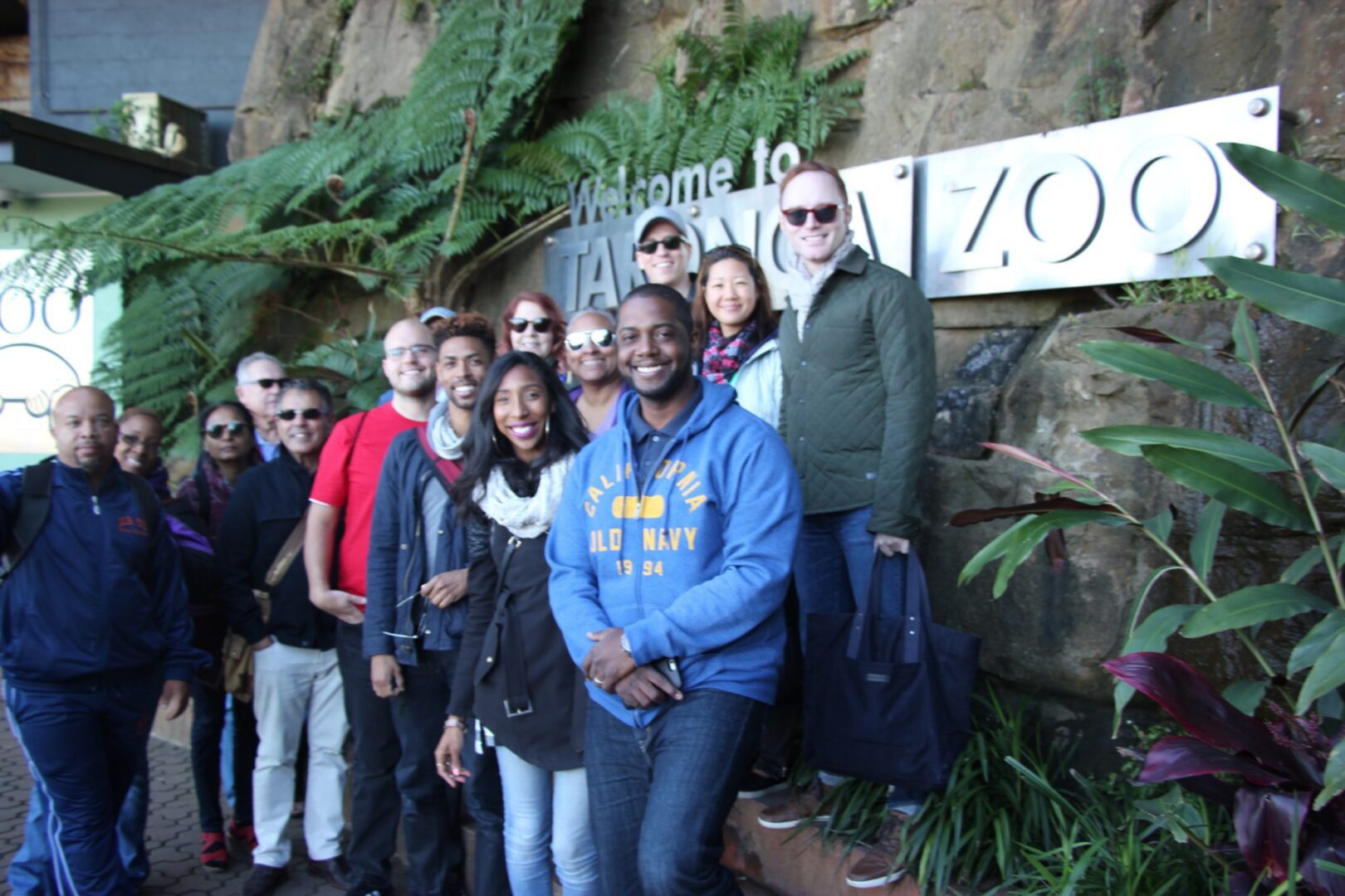 A group of people standing in front of a zoo sign.