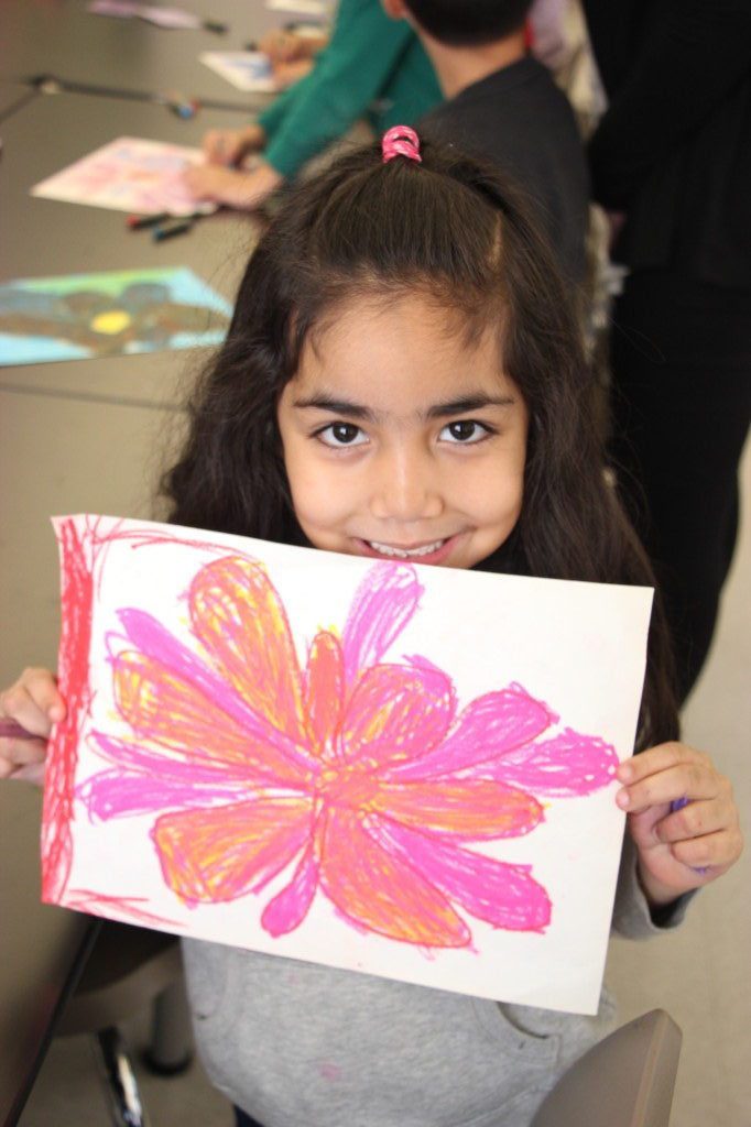 A young girl holding up a flower drawing.