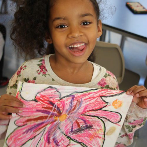 A young girl holding up a flower painting.