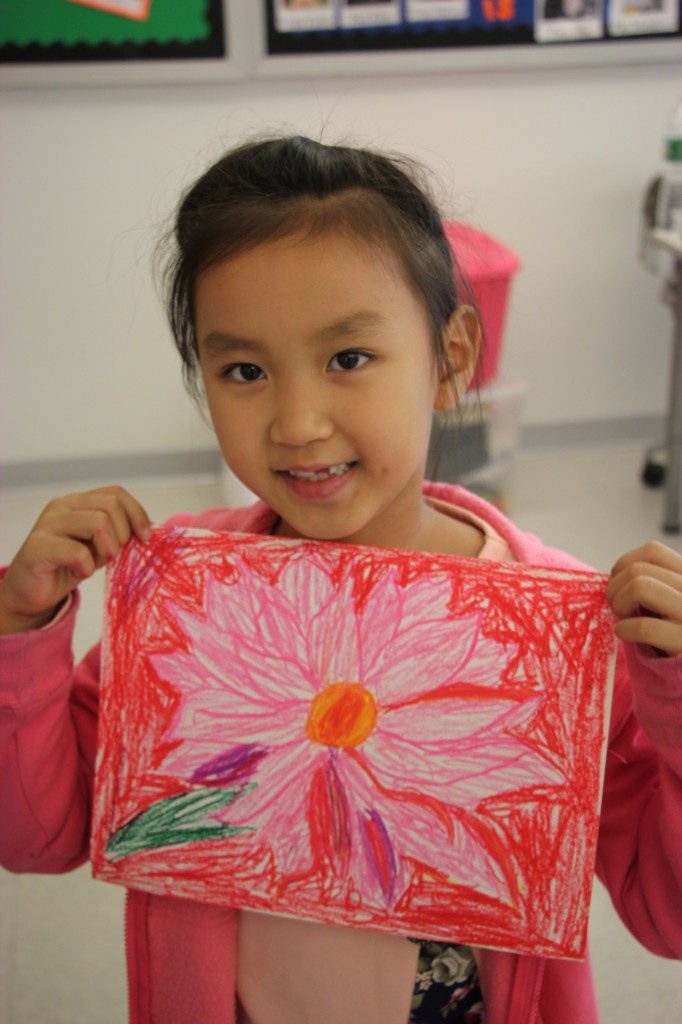 A young girl holding up a drawing of a flower.