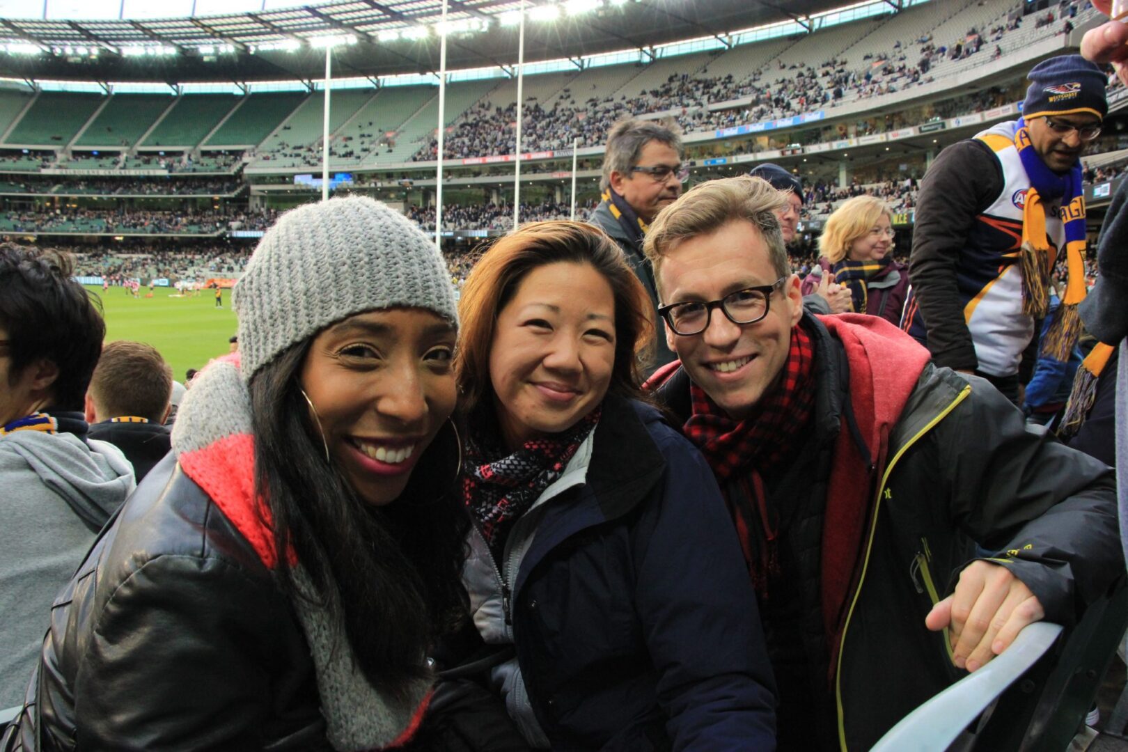 Three people posing for a photo at an afl game.