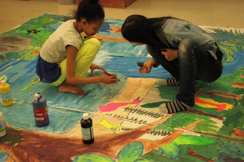 Two girls working on a painting on the floor.
