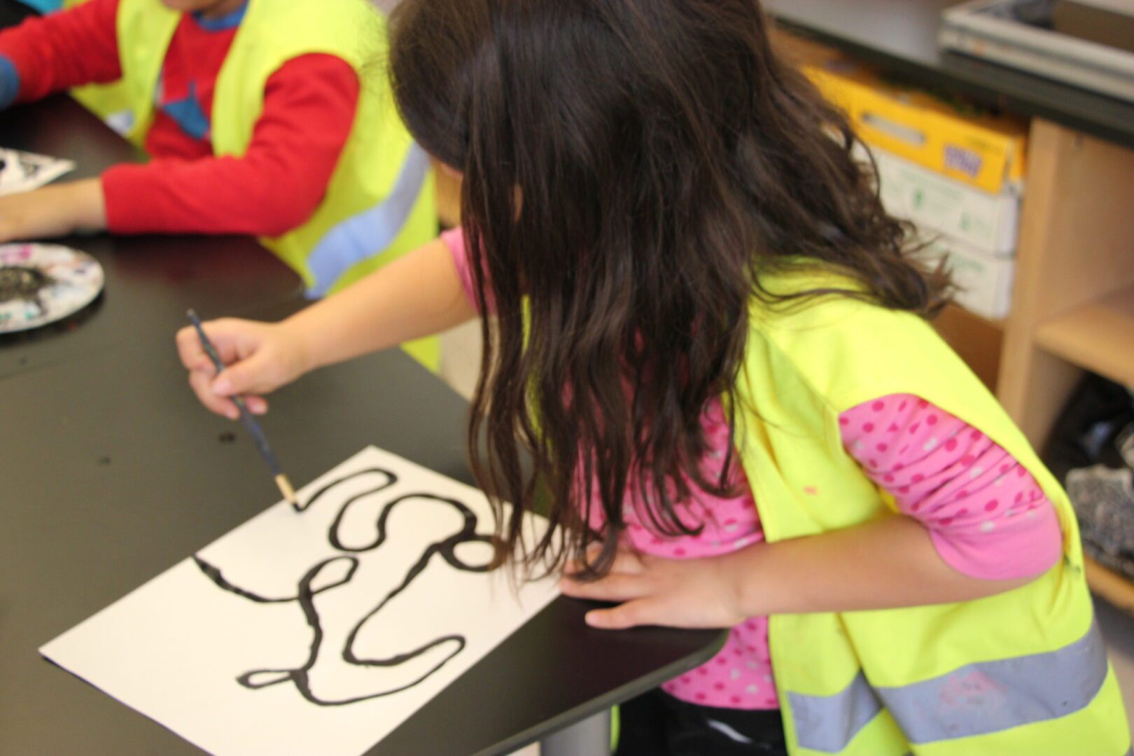 A girl in a yellow vest is drawing on paper.