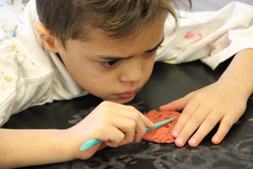 A young boy is making a flower out of clay.