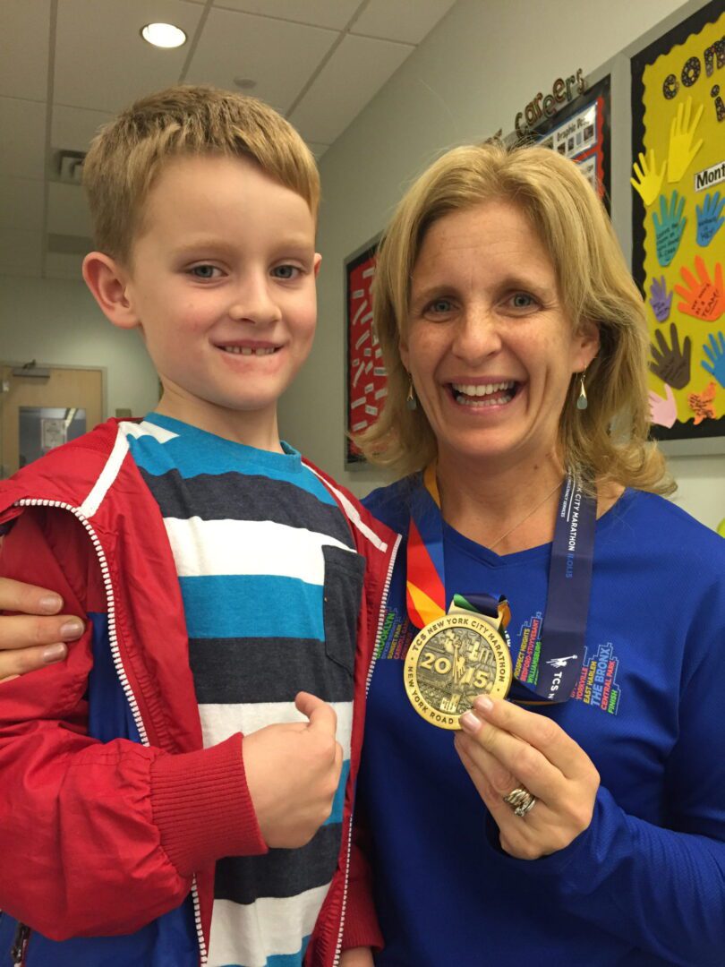 A woman with a boy holding a medal in front of a classroom.