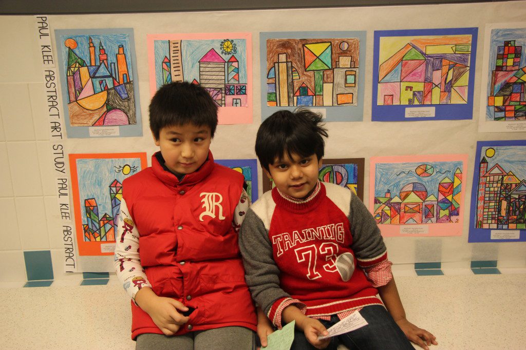 Two boys sitting in front of a wall full of drawings.