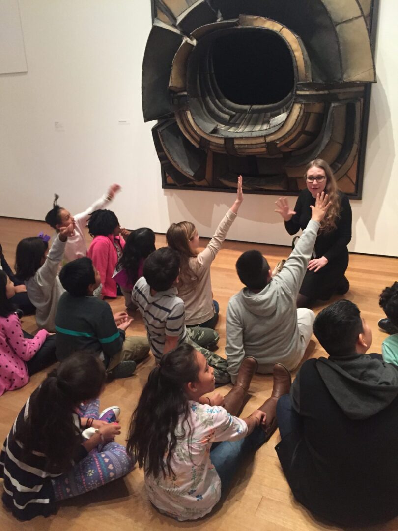 A group of children sitting on the floor in front of a large sculpture.