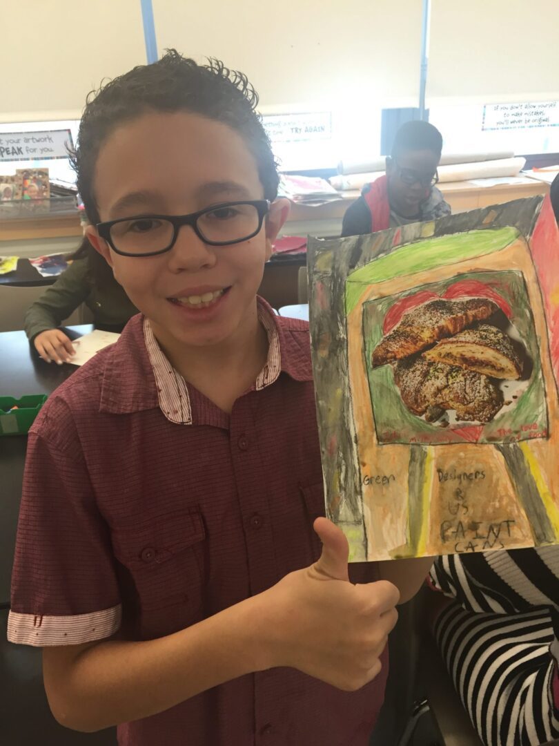 A boy holding up a painting in a classroom.