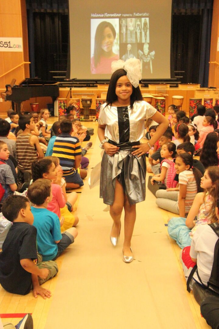 A girl in a silver dress standing in front of a crowd of children.