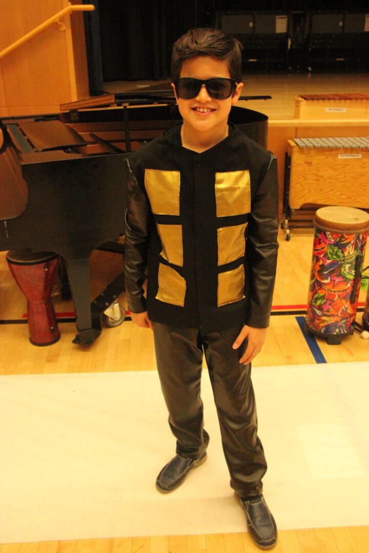 A boy in a black and gold costume standing in front of a piano.