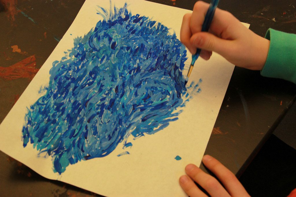 A child is painting with blue paint on a piece of paper.