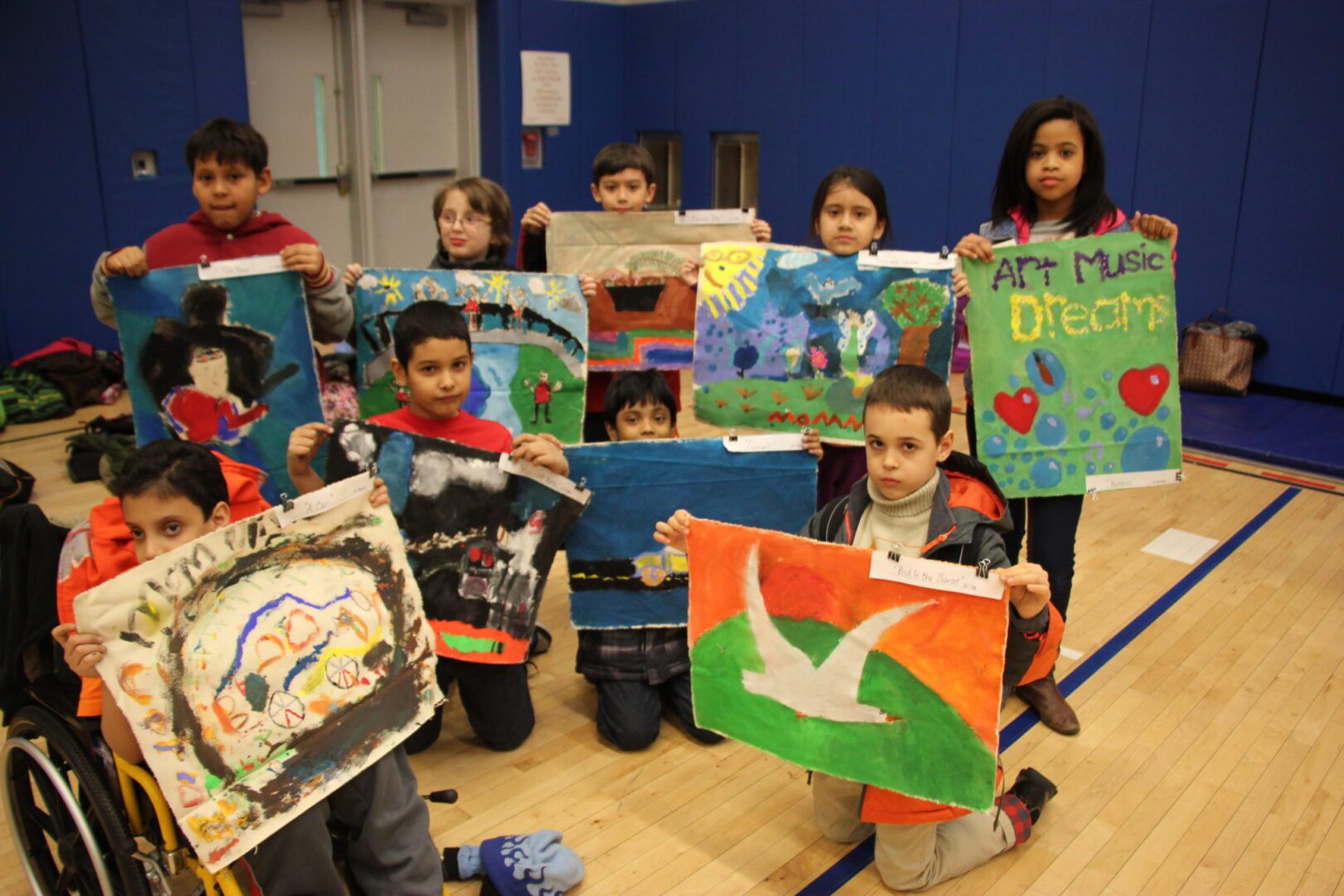 A group of children holding up artwork in a gym.
