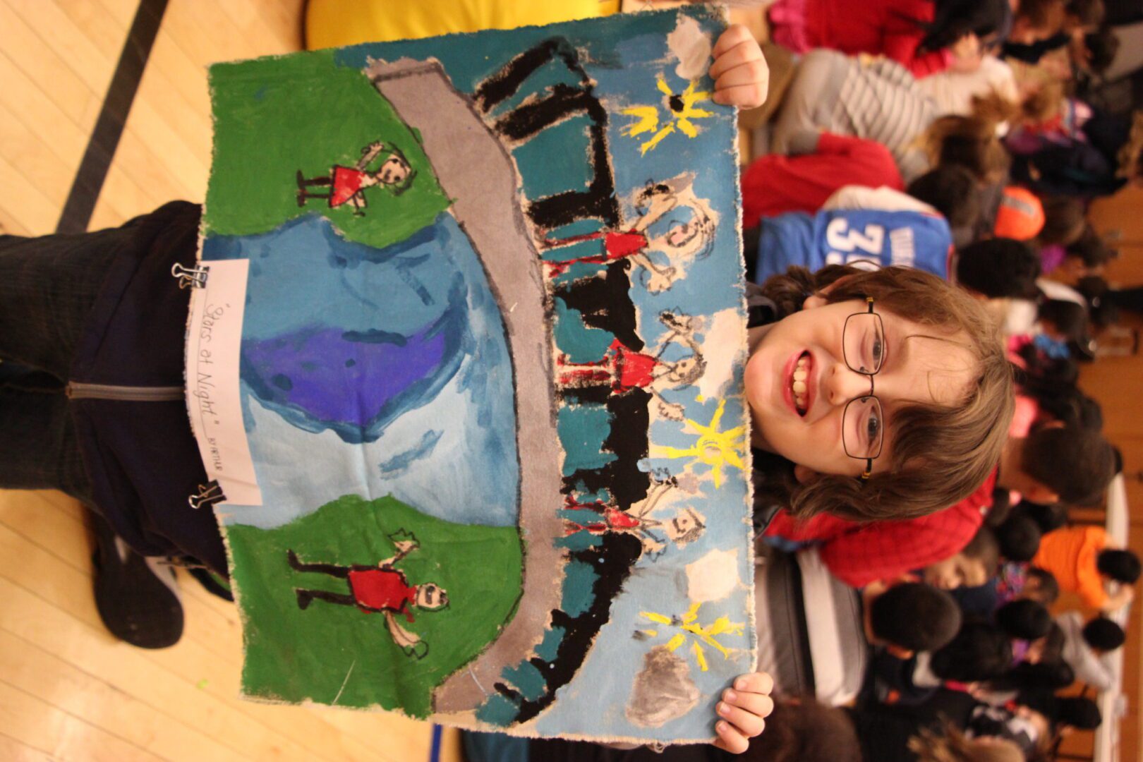 A young girl holding up a drawing in a gym.