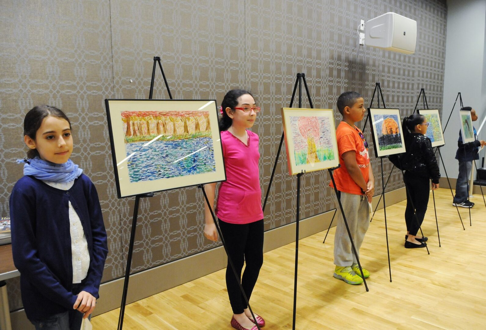 A group of children standing in front of paintings.