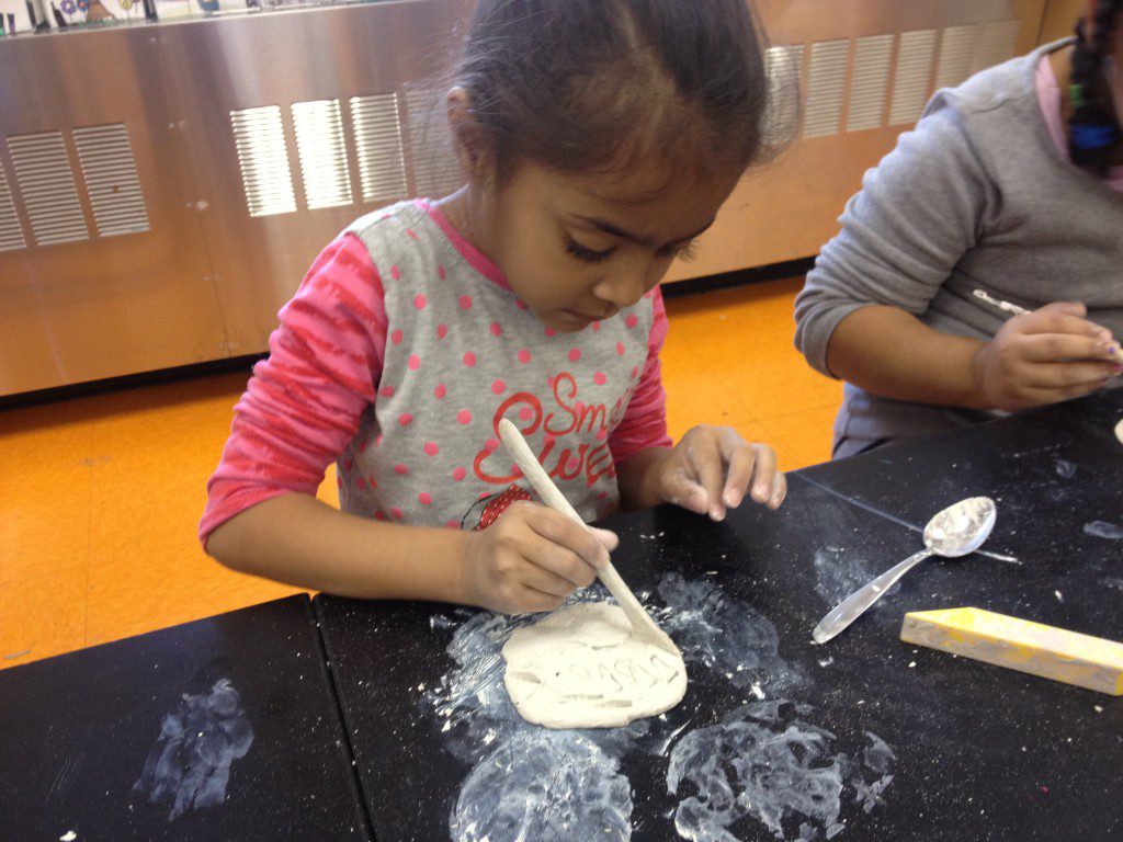 A young girl is making clay with a spoon on a table.