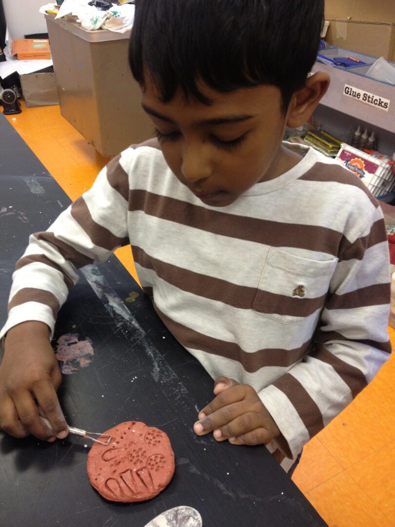 A boy in a striped t-shirt is working on a clay project.