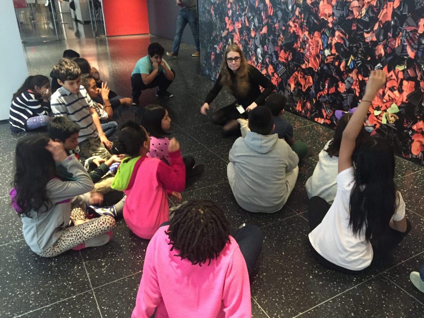 A group of children sitting on the floor in front of a mural.