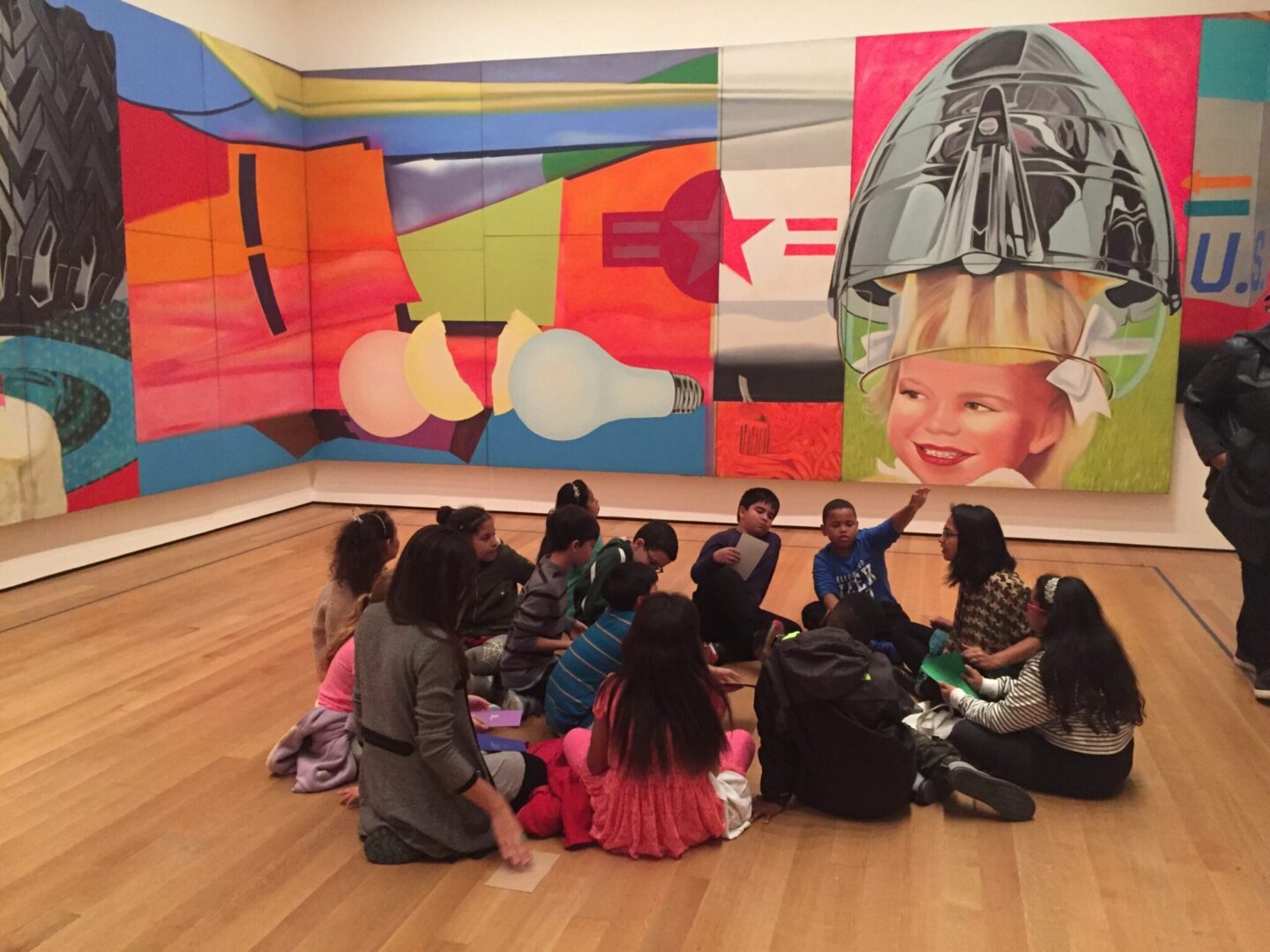 A group of children sitting on the floor in front of paintings.