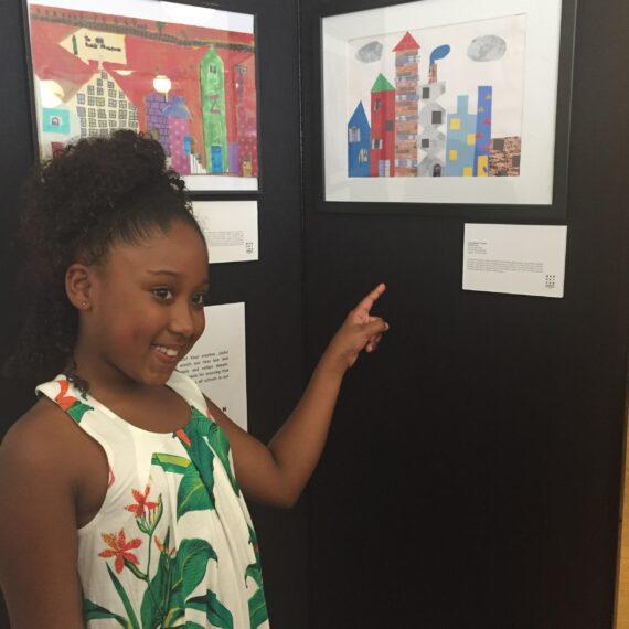 A young girl standing next to a display of artwork.