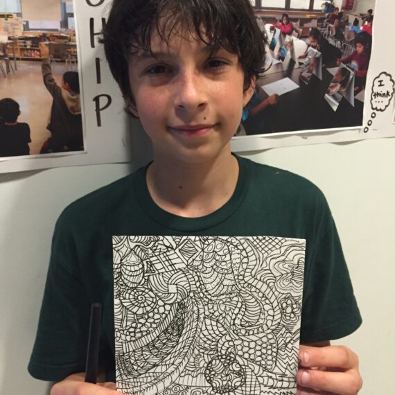 A young boy holding up a drawing.