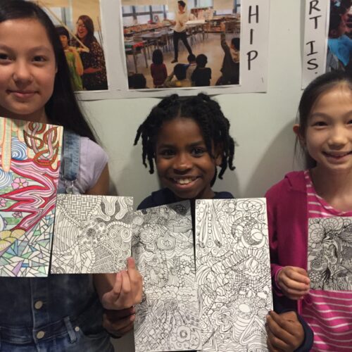 Three young girls holding up drawings in a classroom.