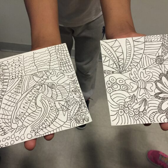 Two people holding up two pieces of paper with designs on them.