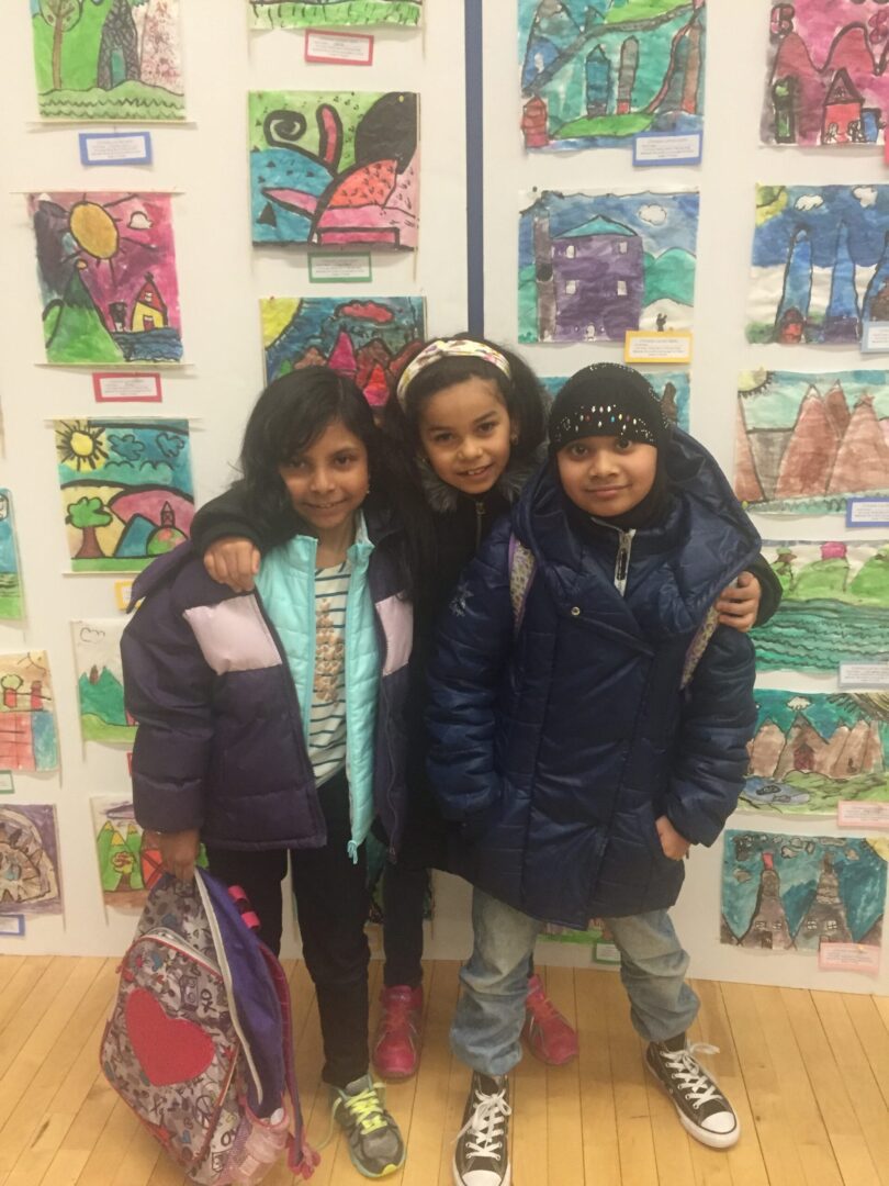 Three young girls posing in front of a wall of art.