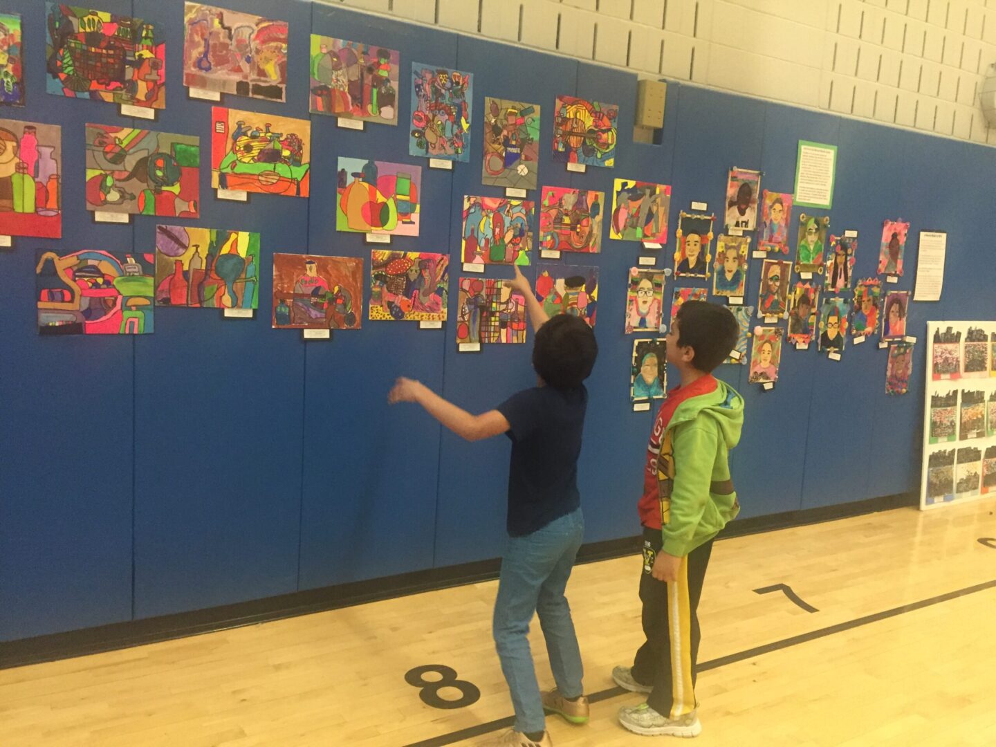 Two children looking at artwork on a wall in a gymnasium.
