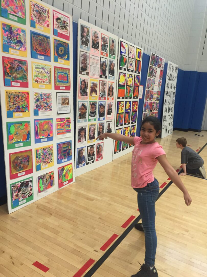 A girl standing in front of a display of art work.