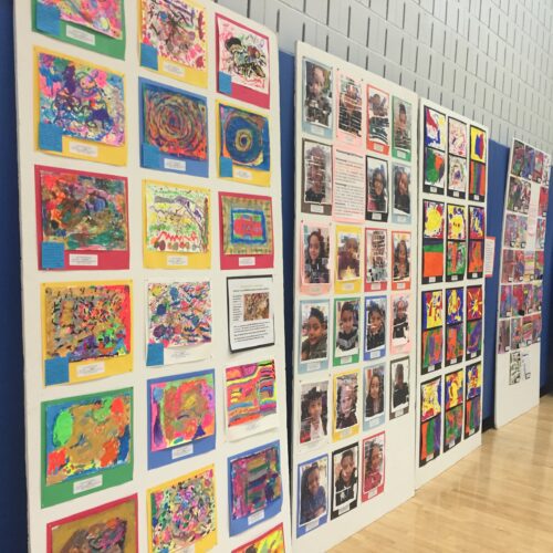 A display of art work on a wall in a gymnasium.