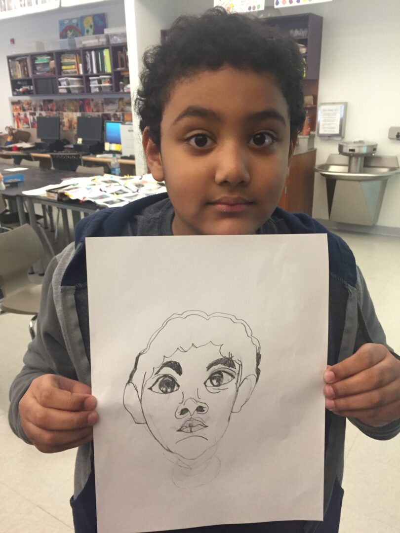 A young boy holding up a drawing of a face.