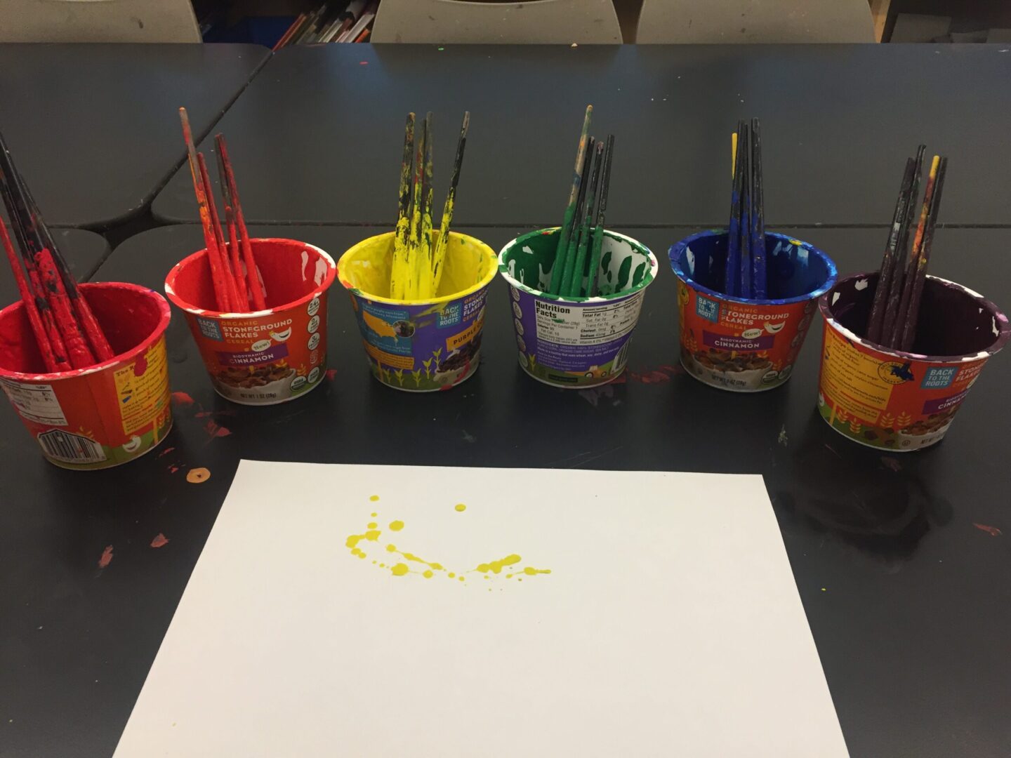 A group of paint brushes on a table next to a piece of paper.