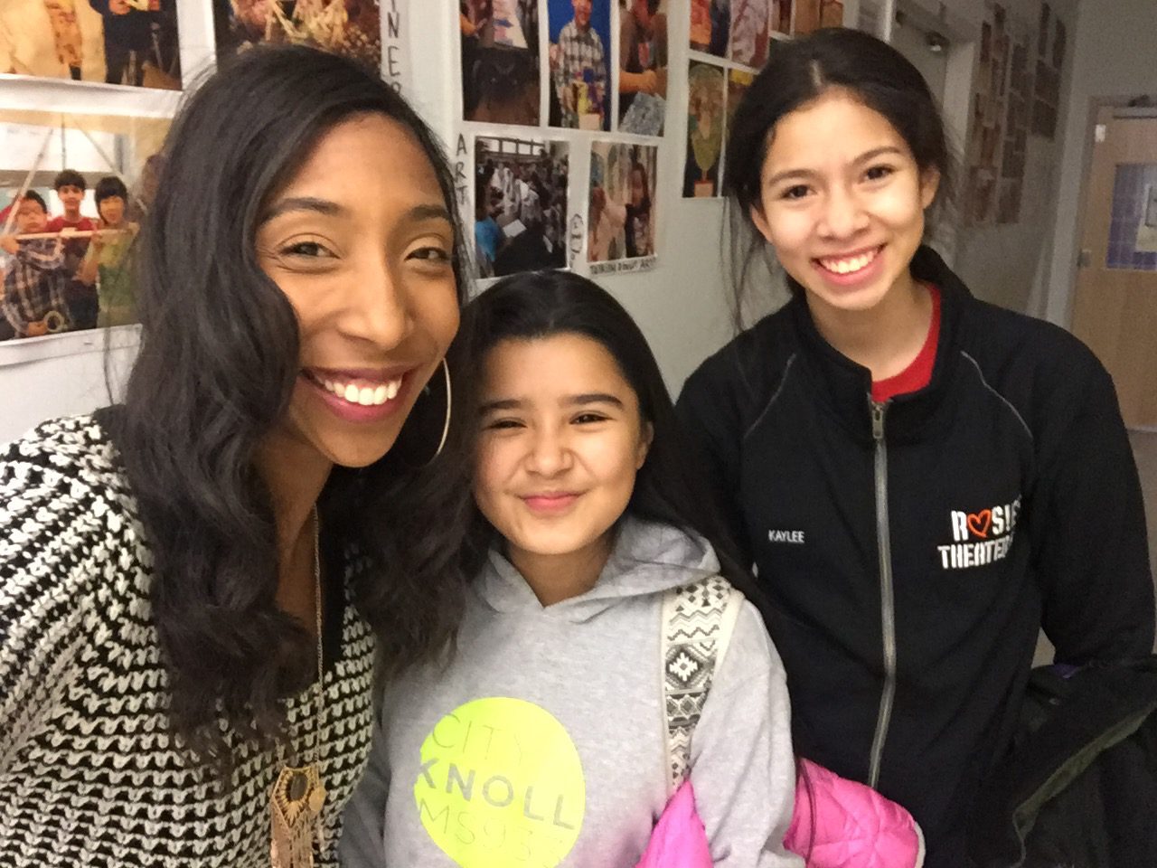 Three young girls posing for a photo in a hallway.