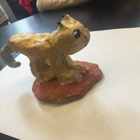 A clay sculpture of a cat sitting on top of a piece of paper.