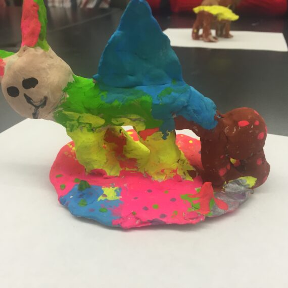 A clay sculpture of a colorful animal on a table.